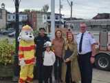 Junior Fire Chief Mia Soutar in front of Municipal Office with parents, Fire Chief Mark Berney, Councillor Guido, and Sparky the Fire Dog